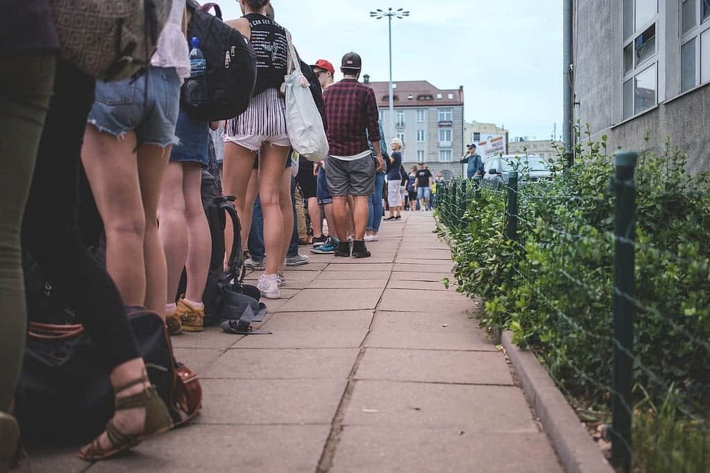people in line next to a building with a small wired fence and small bushes
